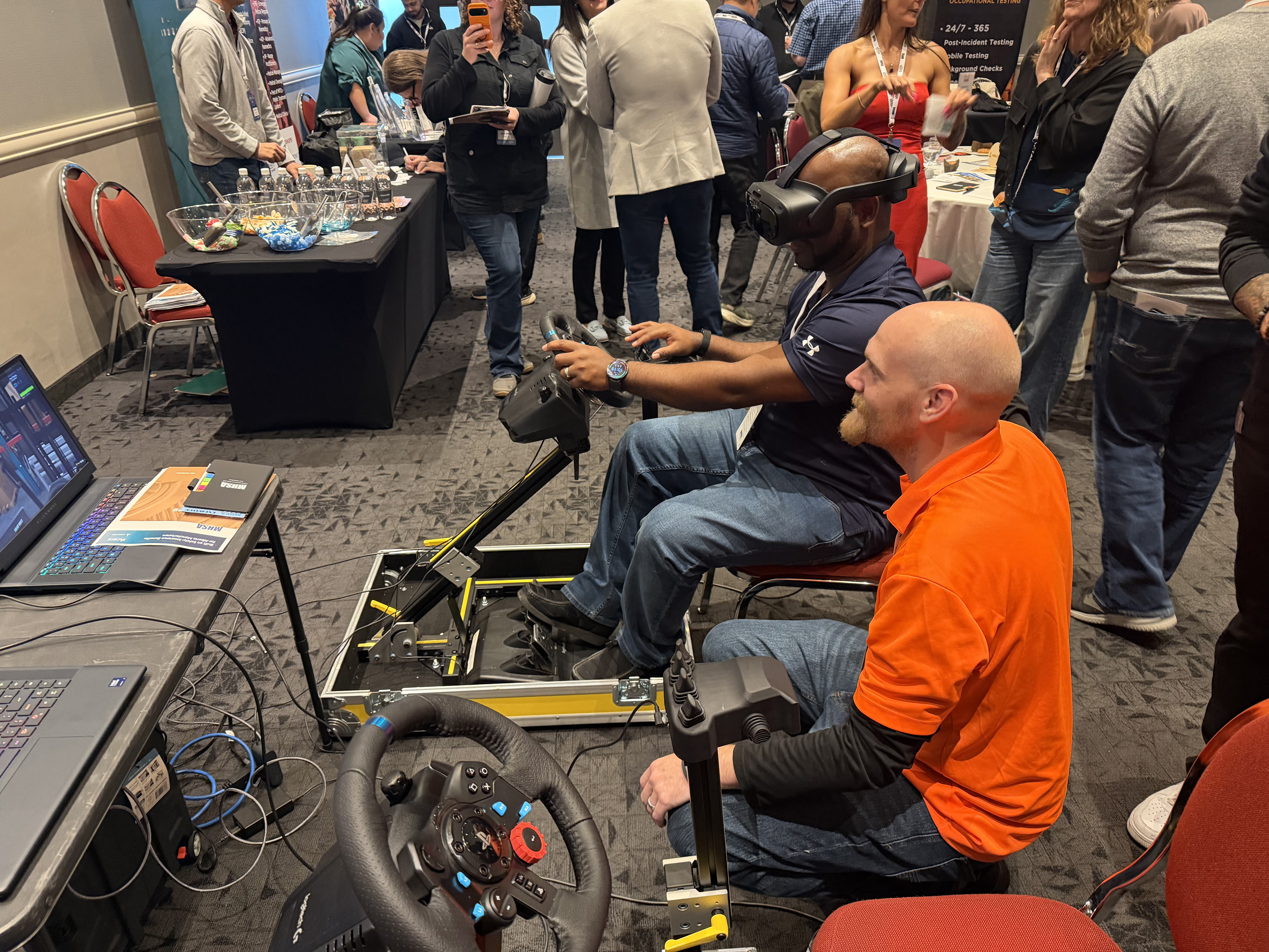 A trainee driving a Fold N Go station in VR while a coach kneels beside him