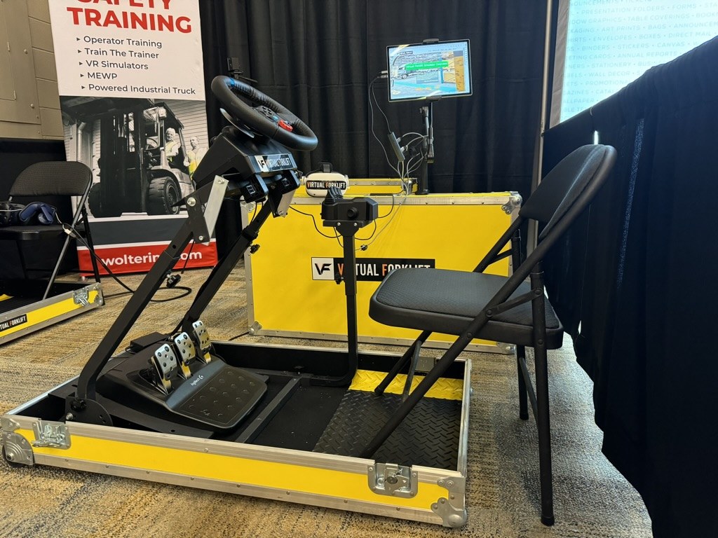 Fold N Go forklift simulator set up in a trade show booth, with steering wheel, pedals, fingertip controls and VR headset